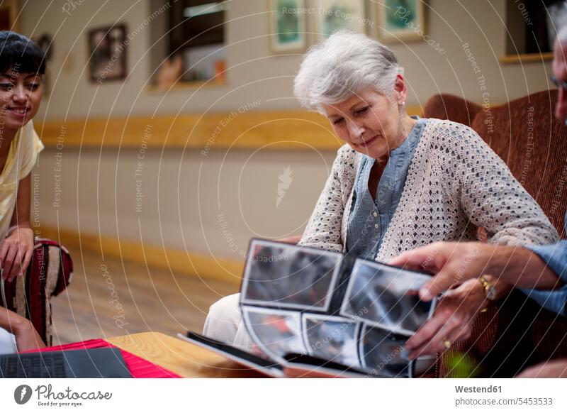 Seniors at retirement home looking at photo albums photograph photographs photos Lounge recreation room common room senior women elder women elder woman old