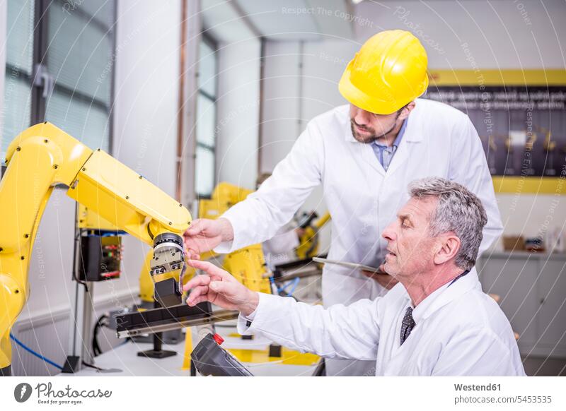 Two engineers examining industrial robot man men males colleagues Robot factory factories Adults grown-ups grownups adult people persons human being humans