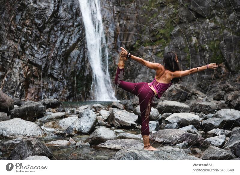 Italy, Lecco, woman doing Lord of the Dance Yoga Pose on a rock near a waterfall yoga females women waterfalls standing mindfulness aware awareness self-care