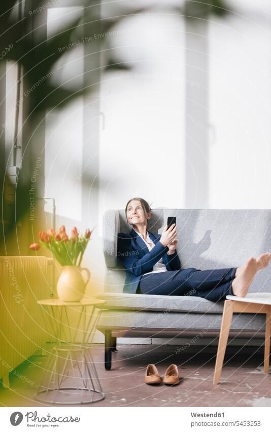 Businesswoman sitting on couch in a loft looking out of the window businesswoman businesswomen business woman business women females business people