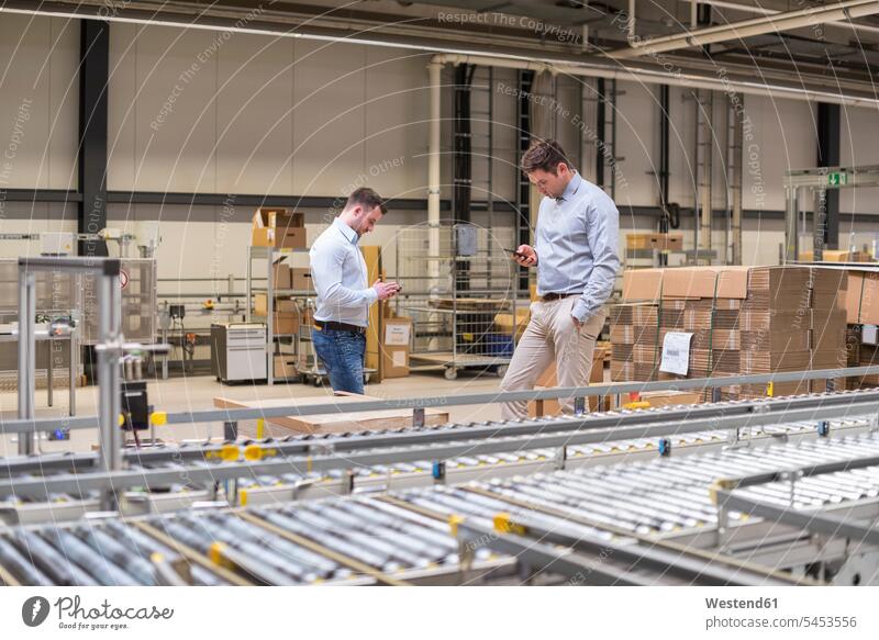 Two men at conveyor belt in factory looking at cell phones Businessman Business man Businessmen Business men mobile phone mobiles mobile phones Cellphone