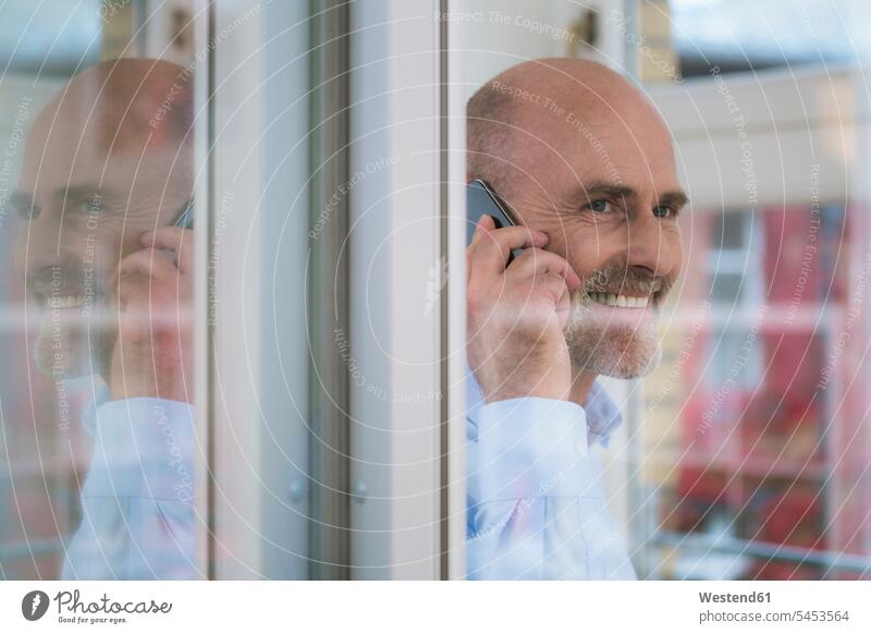 Smiling businessman on cell phone at the window smiling smile mobile phone mobiles mobile phones Cellphone cell phones on the phone call telephoning
