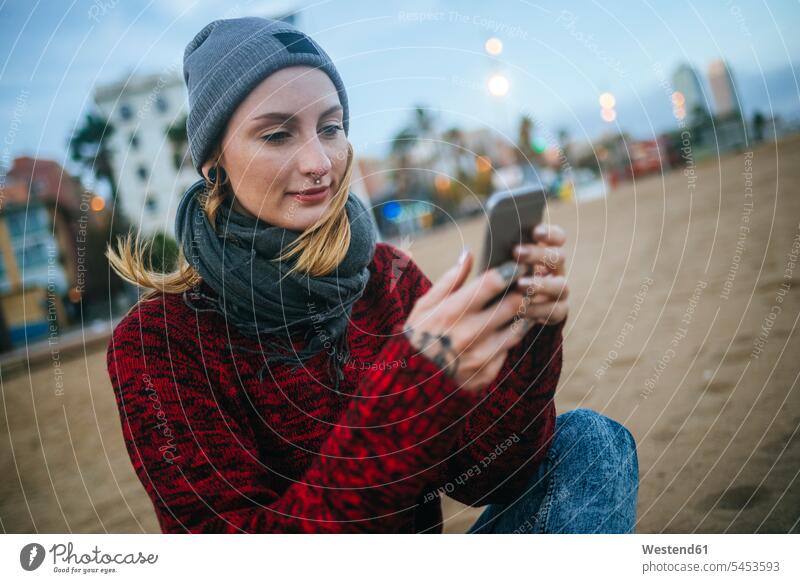 Young woman sitting on the beach in winter using cell phone beaches females women Seated mobile phone mobiles mobile phones Cellphone cell phones Adults