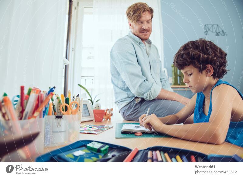 Father helping boy doing his schoolwork at home father pa fathers daddy dads papa explaining homework Home work son sons manchild manchildren parents family