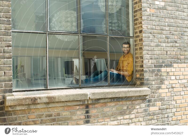 Young professional at the window looking confident, using laptop window sill windowsill sills window sills Window Cill windowsills Businessman Business man