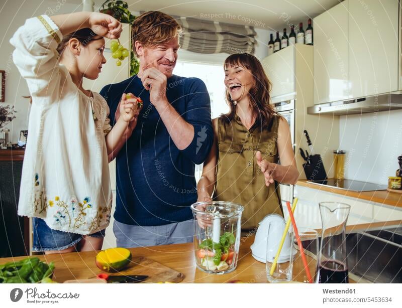 Parents and daughter tasting fruit for a smoothie kitchen Fun having fun funny family families daughters people persons human being humans human beings child