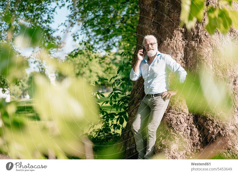 Mature man on cell phone leaning against tree portrait portraits Tree Trees on the phone call telephoning On The Telephone calling mobile phone mobiles
