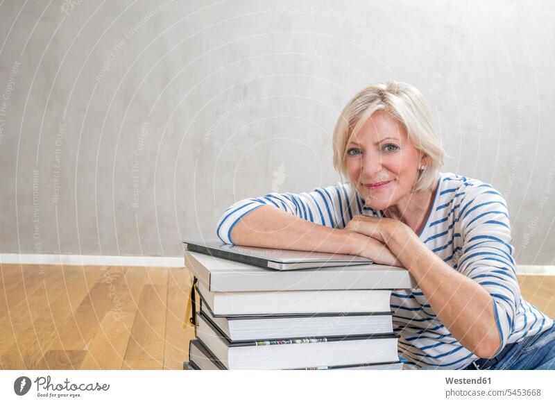Portrait of smiling senior woman leaning on stack of books and laptop portrait portraits stacked stacks Laptop Computers laptops notebook smile senior women