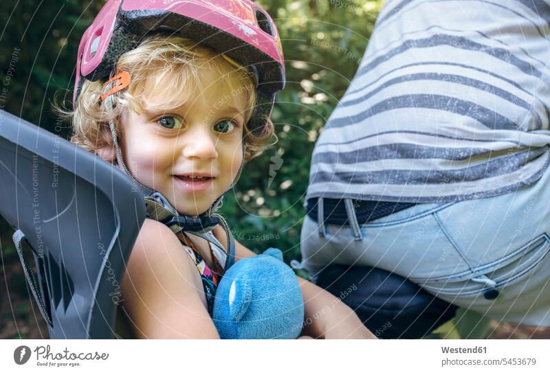 Portrait of little girl with helmet sitting on a child seat for bicycle with her father helmets Protective Headwear bikes bicycles smiling smile females girls