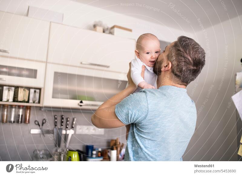 Father holding and kissing baby son in kitchen father pa fathers daddy dads papa infants nurselings babies domestic kitchen kitchens kisses parents family