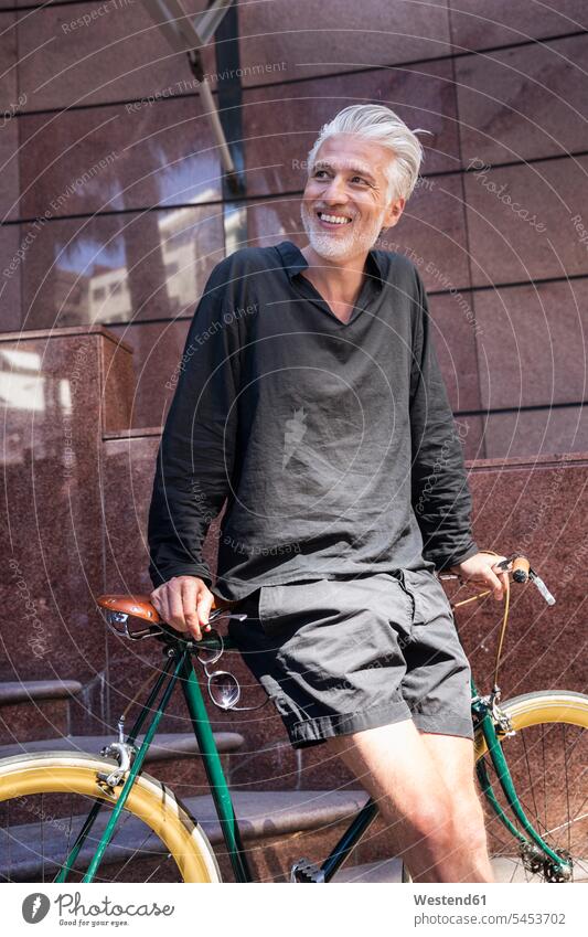 Mature man in the city leaning on his bicycle bikes bicycles men males riding bicycle riding bike bike riding cycling bicycling pedaling on the move on the way