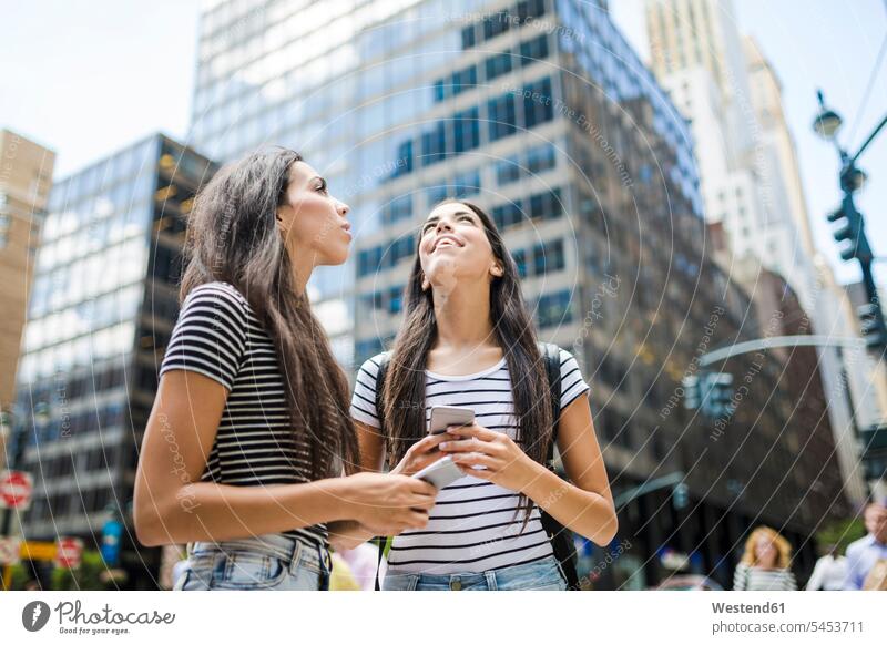 USA, New York City, two twin sisters with cell phones in Manhattan looking up female friends mobile phone mobiles mobile phones Cellphone Fun having fun funny