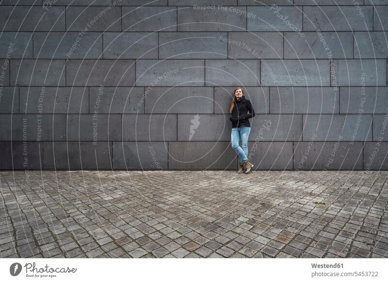 Young woman standing in front of grey facade waiting females women Adults grown-ups grownups adult people persons human being humans human beings Facade Facades