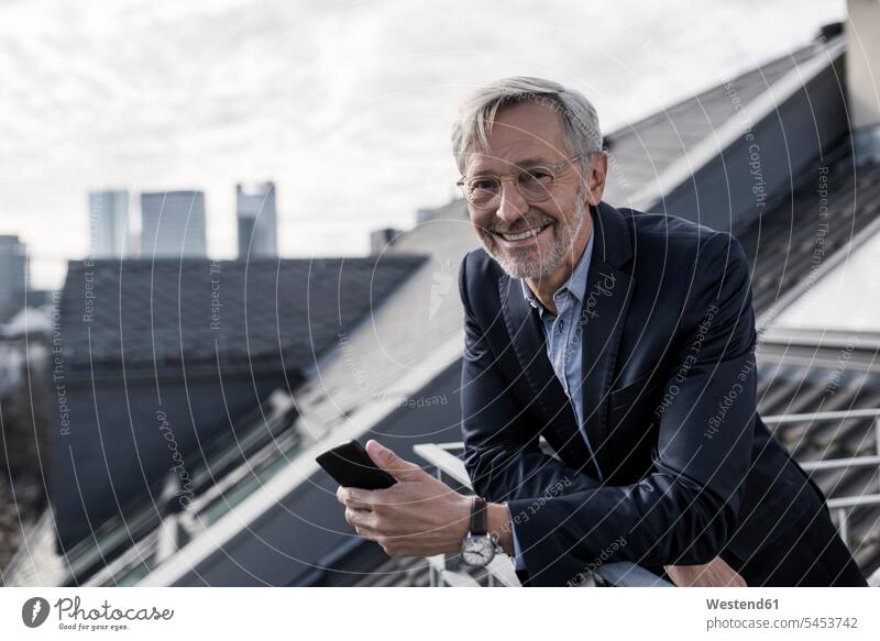 Grey-haired businessman on balcony holding smartphone smiling into camera smile Businessman Business man Businessmen Business men mobile phone mobiles
