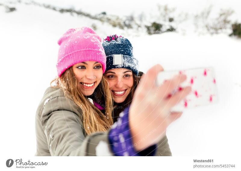 Two friends taking smart phone selfies in the snow winter hibernal friendship mobile phone mobiles mobile phones Cellphone cell phone cell phones laughing
