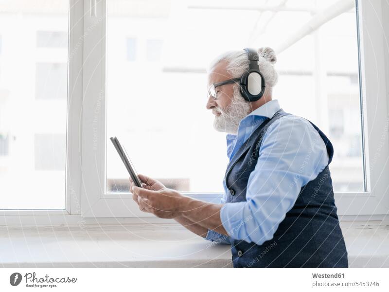 Mature man with tablet and headphones at the window hearing windows headset men males digitizer Tablet Computer Tablet PC Tablet Computers iPad Digital Tablet