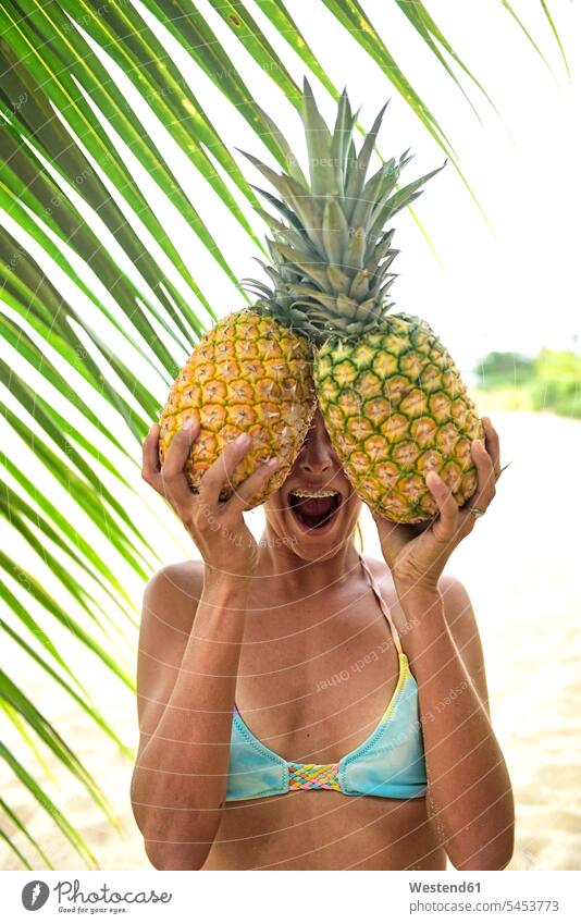 Young woman holding two pineapples at palm tree Pineapple Ananas comosus Ananas sativus Pineapples Fun having fun funny females women laughing Laughter Fruit