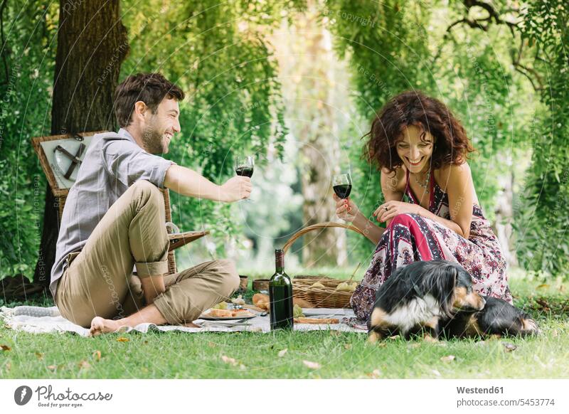 Couple with dog having a picnic in a park drinking red wine dogs Canine Picnic picnicking parks smiling smile couple twosomes partnership couples Wine pets