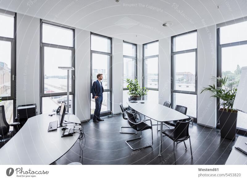 Businessman standing in his office looking out of the window Business man Businessmen Business men offices office room office rooms business people