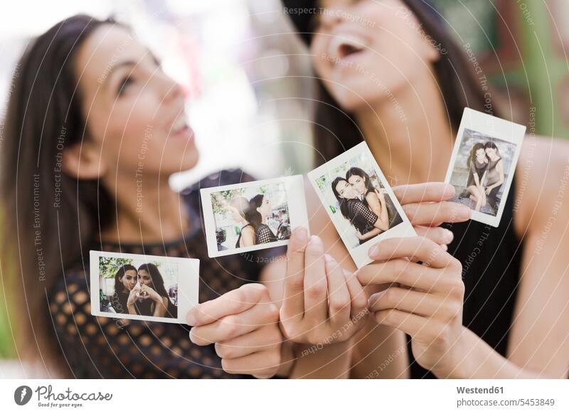 Two happy twin sisters holding instant photos of themselves photograph photographs female friends image images picture pictures mate friendship siblings