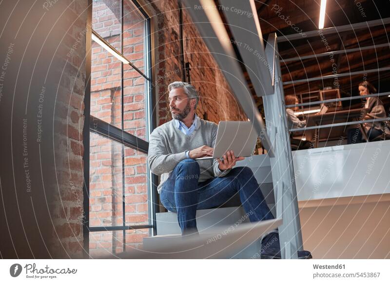 Businessman sitting on stairs of modern office, using laptop contemporary working At Work offices office room office rooms loft lofts Business man Businessmen