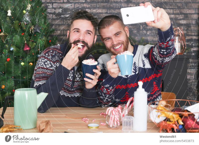 Happy gay couple taking selfie with smartphone at Christmas time at home Selfie Selfies portrait portraits Gay Couple Gays same-sex couple woman and woman