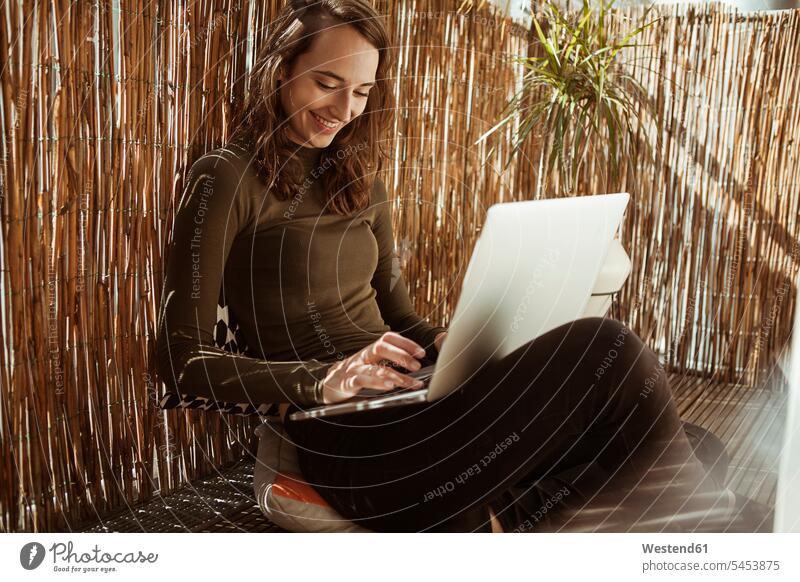Smiling young woman sitting on balcony using laptop smiling smile Laptop Computers laptops notebook Seated females women computer computers Adults grown-ups