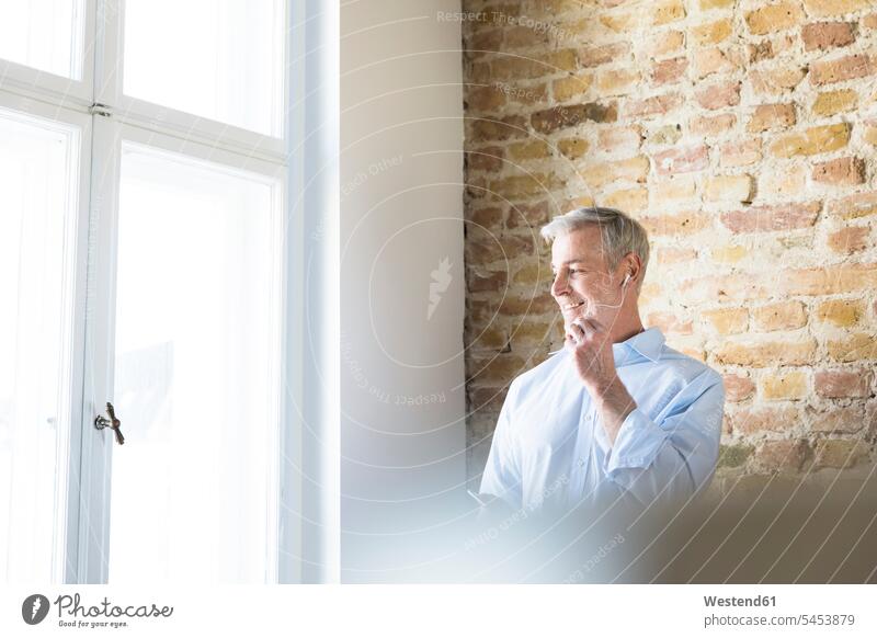 Businessman in office at the window using hands-free phone on the phone call telephoning On The Telephone calling Business man Businessmen Business men smiling
