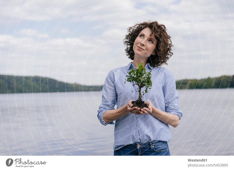 Woman at lake holding little tree in her hands nature protection nature conservation woman females women Tree Trees lakes environmental issues ecology