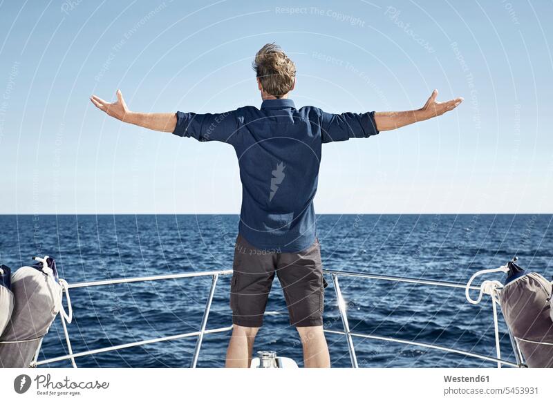 Back view of mature man standing on his motor yacht with arms outstretched Sea ocean men males motor yachts water Adults grown-ups grownups adult people persons