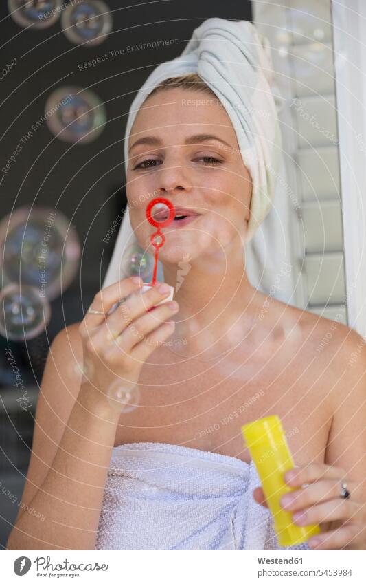 Happy young woman wrapped in a towel blowing soap bubbles females women Adults grown-ups grownups adult people persons human being humans human beings towels