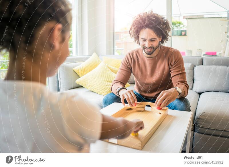 Father and daughter sitting on couch playing foosball Seated father pa fathers daddy dads papa settee sofa sofas couches settees Concentration concentrating