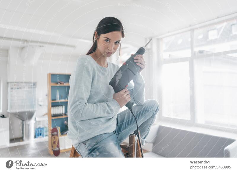 Young woman in her new flat sitting on ladder, holding electric drill females women young moving house move Moving Home mounting assembling loft lofts