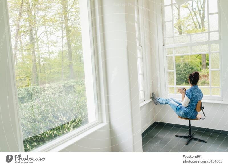 Woman with cup of coffee sitting on chair at the window woman females women drinking relaxed relaxation windows Coffee Adults grown-ups grownups adult people