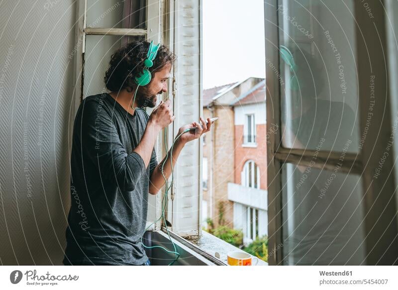 Man talking on cell phone in his room by the window man men males headphones headset Adults grown-ups grownups adult people persons human being humans