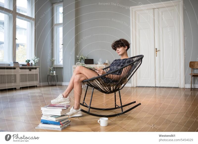 Young woman sitting on rocking chair at home reading a book books females women Adults grown-ups grownups adult people persons human being humans human beings