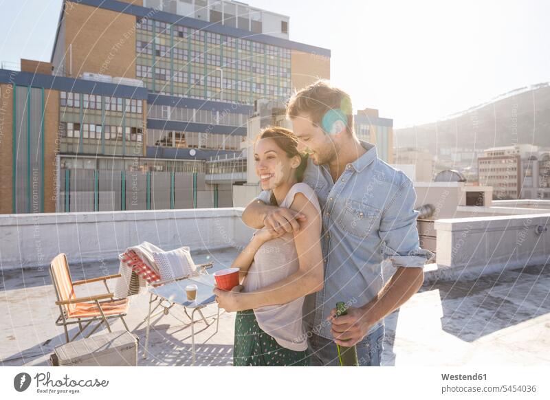 Young couple celebrating on a rooftop terrace, embracing at sunset Mixed Race Person mixed-race Person mixed race ethnicity Fun having fun funny leisure