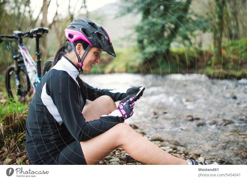 Smiling woman with mountain bike resting in nature checking her cell phone females women mobile phone mobiles mobile phones Cellphone cell phones