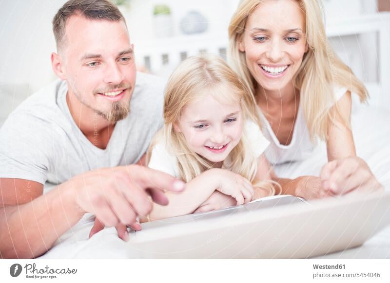 Smiling girl with parents lying in bed using laptop beds family families daughter daughters smiling smile Laptop Computers laptops notebook people persons