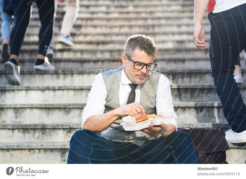 Businessman in the city sitting on stairs eating a hamburger Business man Businessmen Business men stairway break business people businesspeople business world