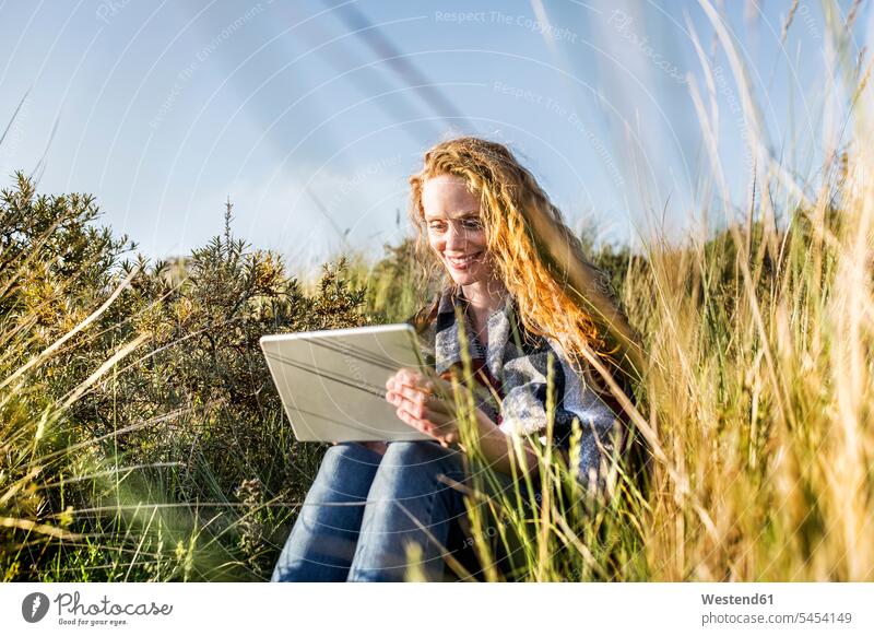 Netherlands, Zandvoort, smiling woman sitting in dunes with tablet digitizer Tablet Computer Tablet PC Tablet Computers iPad Digital Tablet digital tablets