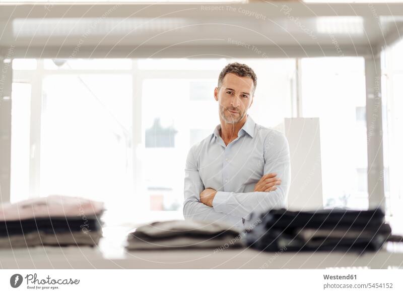 Portrait of confident businessman standing at shelf with clothes Apparel Businessman Business man Businessmen Business men portrait portraits business people