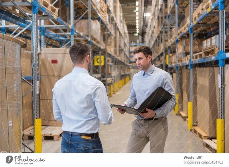 Two men with folder talking in factory warehouse speaking working At Work colleagues storehouse storage man males dumps stock Adults grown-ups grownups adult