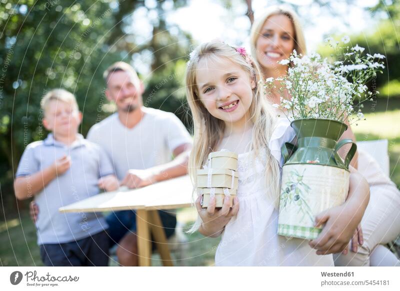 Portrait of smiling girl outdoors holding jug and boxes with family in background Flower Flowers smile jar jugs jars Plant Plants families people persons