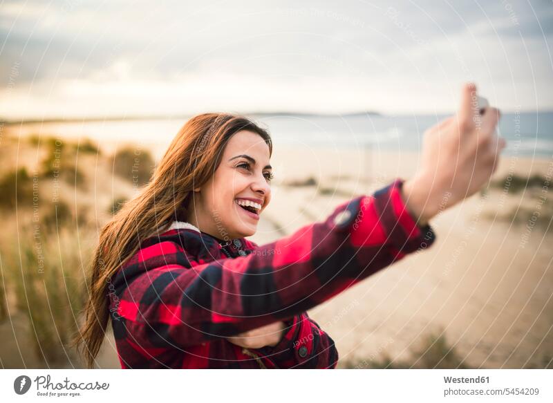 Laughing young woman taking selfie with smartphone on the beach Selfie Selfies beaches females women Adults grown-ups grownups adult people persons human being