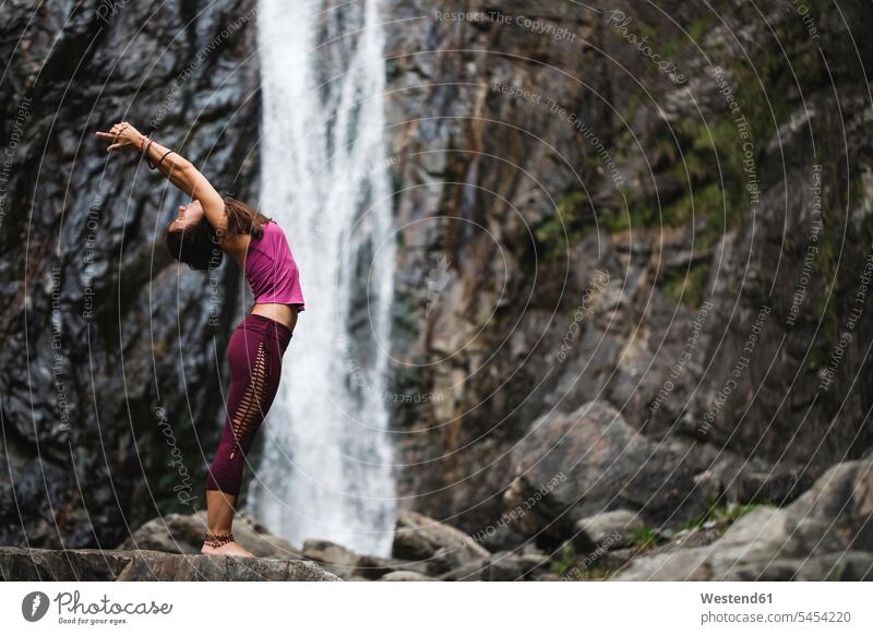 Italy, Lecco, woman doing Standing Backbend Yoga Pose on a rock near a waterfall yoga females women waterfalls standing mindfulness aware awareness self-care