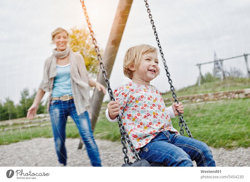 Mother with daughter on swing on playground swing set swingset laughing Laughter mother mommy mothers ma mummy mama daughters play yard play ground playgrounds