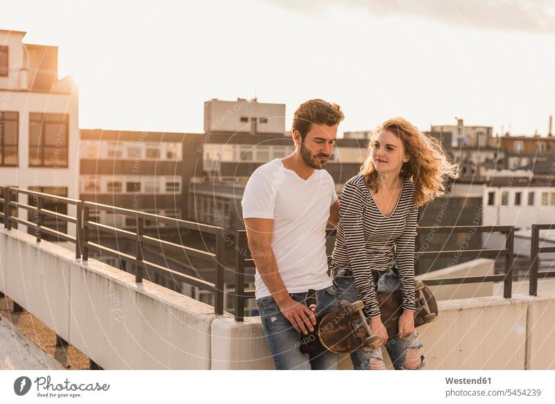 Young couple relaxing on roof terrace at sunset twosomes partnership couples sunsets sundown relaxation deck rooftop people persons human being humans