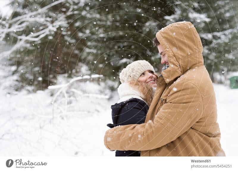 Happy young couple standing face to face in snow-covered winter forest twosomes partnership couples people persons human being humans human beings happiness