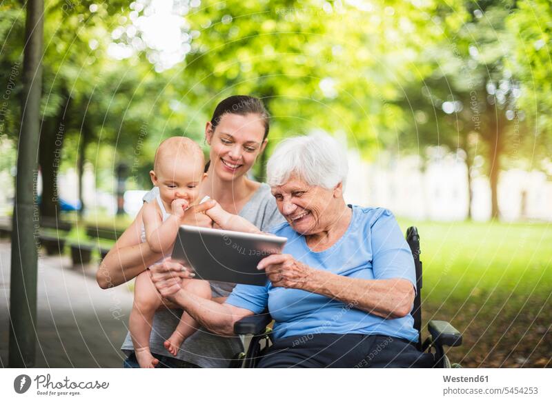 Grandmother, daughter and granddaughter having fun with tablet in a park parks grandmother grandmas grandmothers granny grannies Fun funny granddaughters